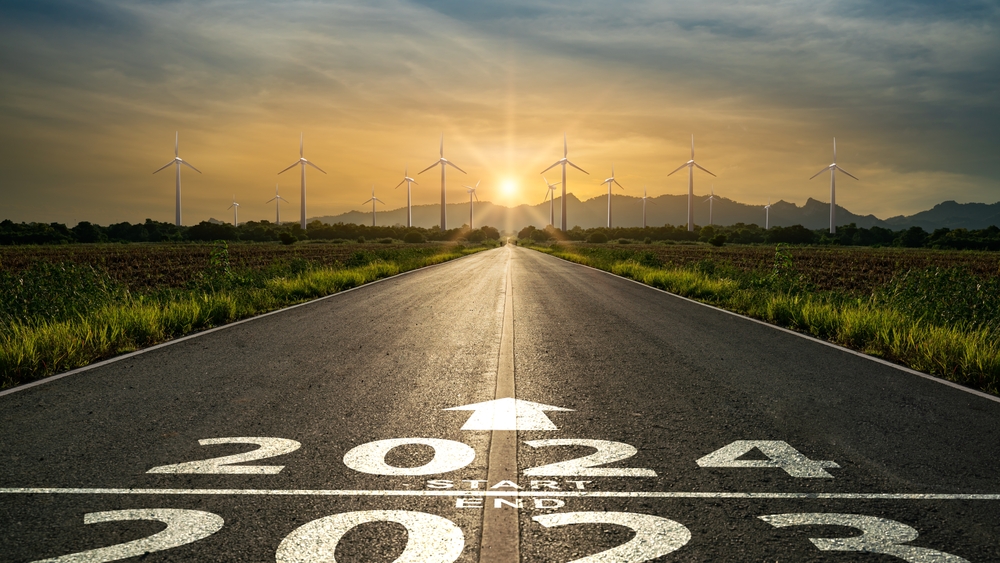 road turning from 2023 toward 2024 with sun and wind turbines in distance