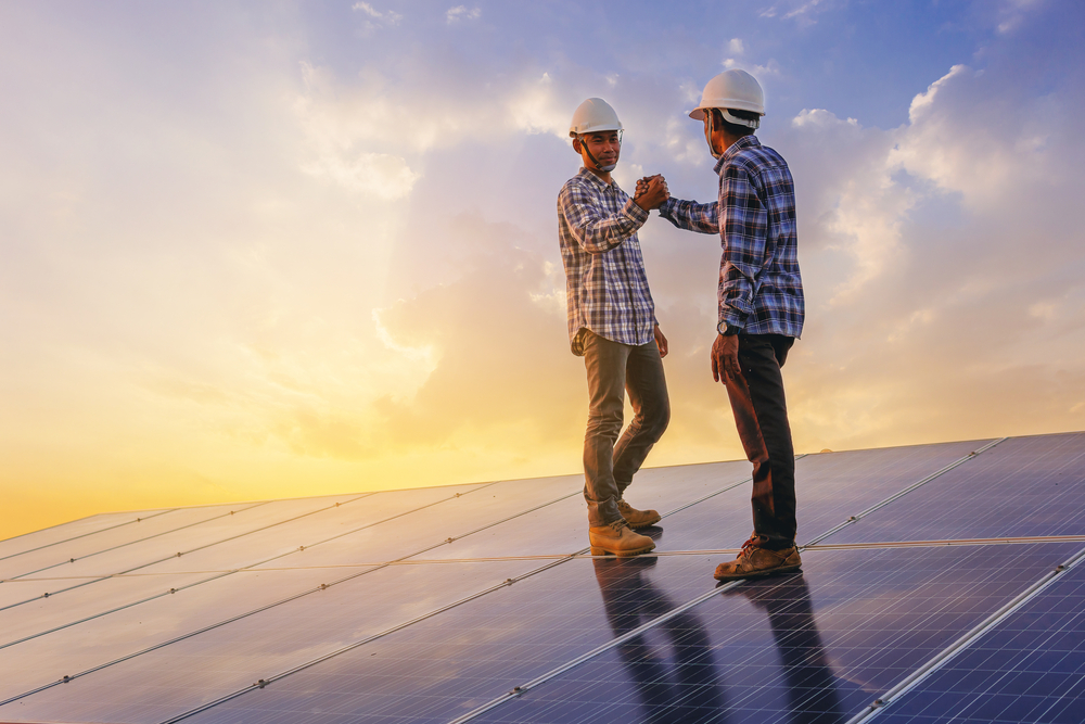 Two hardhat workers celebrate on solar panels with sun in background