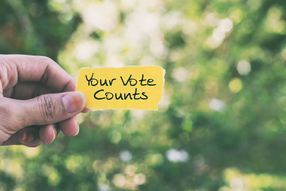 Your Vote Counts on yellow paper with green foliage in background