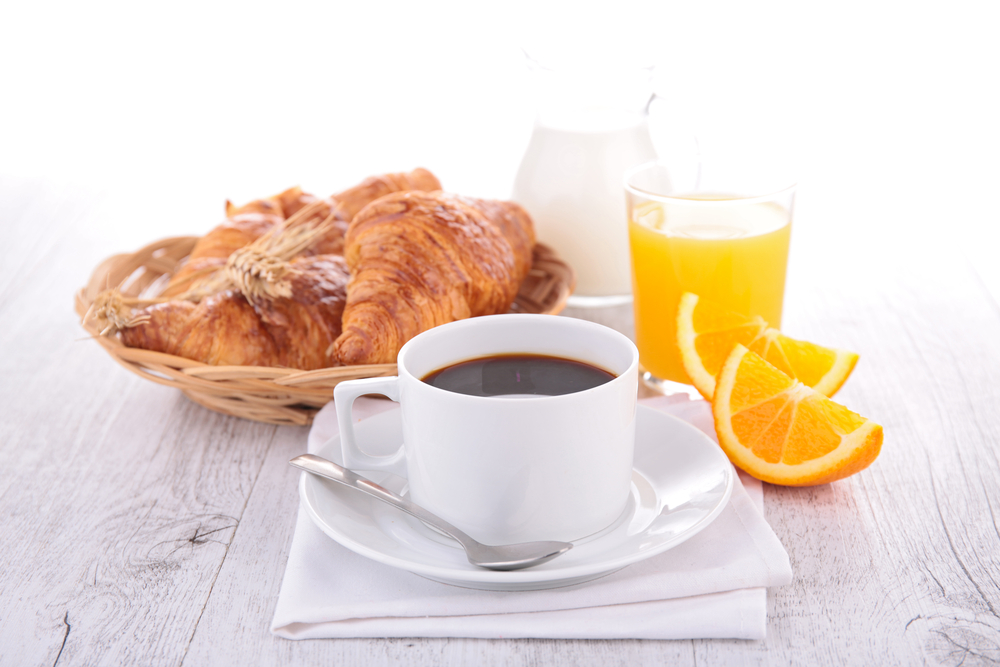 Cup of coffee, orange slices, juice and croissant on table