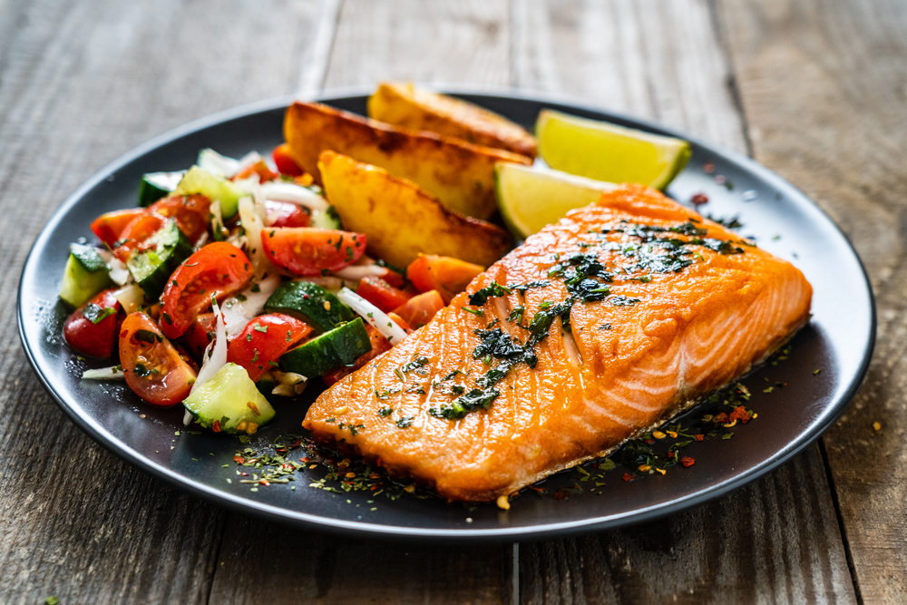 Grilled salmon and tomato salad with lime and grilled potato clices on a silver plate