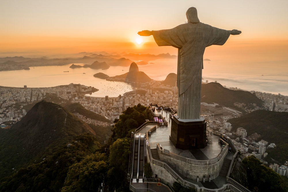 Rio de Janeiro, Brazil - March 21, 2023: Christ the Redeemer statue on top of the Corcovado Mountain with the Sugarloaf Mountain in the horizon on sunrise.