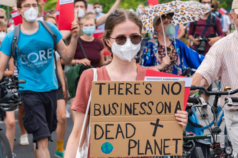 Young adult and chldren protestors wearing masks with sign in front saying "There's no business on a Dead Planet"