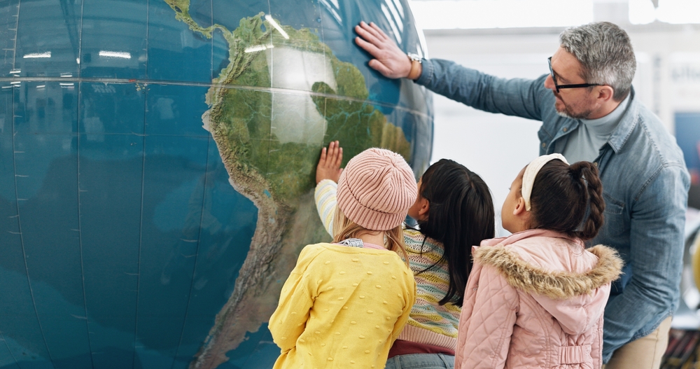 Male science teacher with three children facing large globe