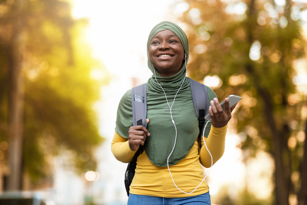 image of a smiling woman in a hijab listening to something from her phone through headphones