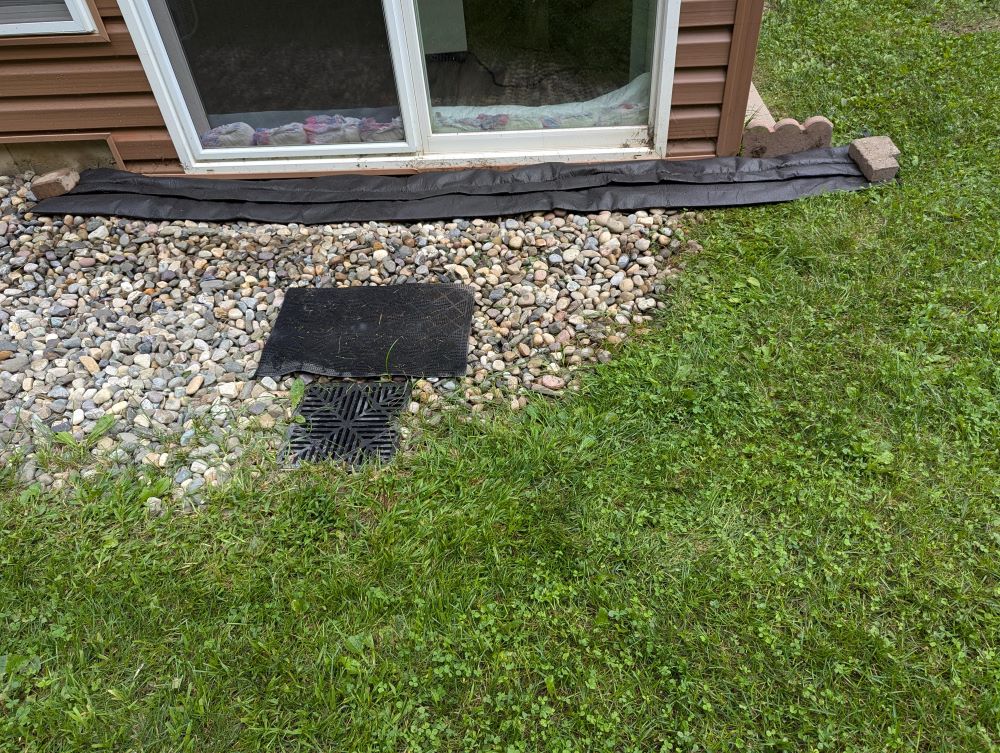 photo outside sunroom sliding doors with black flood barrier in place and French drain below