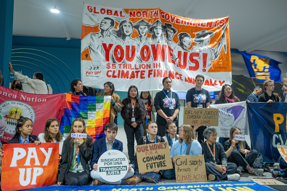 Protestors at COP29 with sign saying "Global North Governments - You Owe Us $5 Tillion in Climate Finance" and "Our Money for a Common Future"