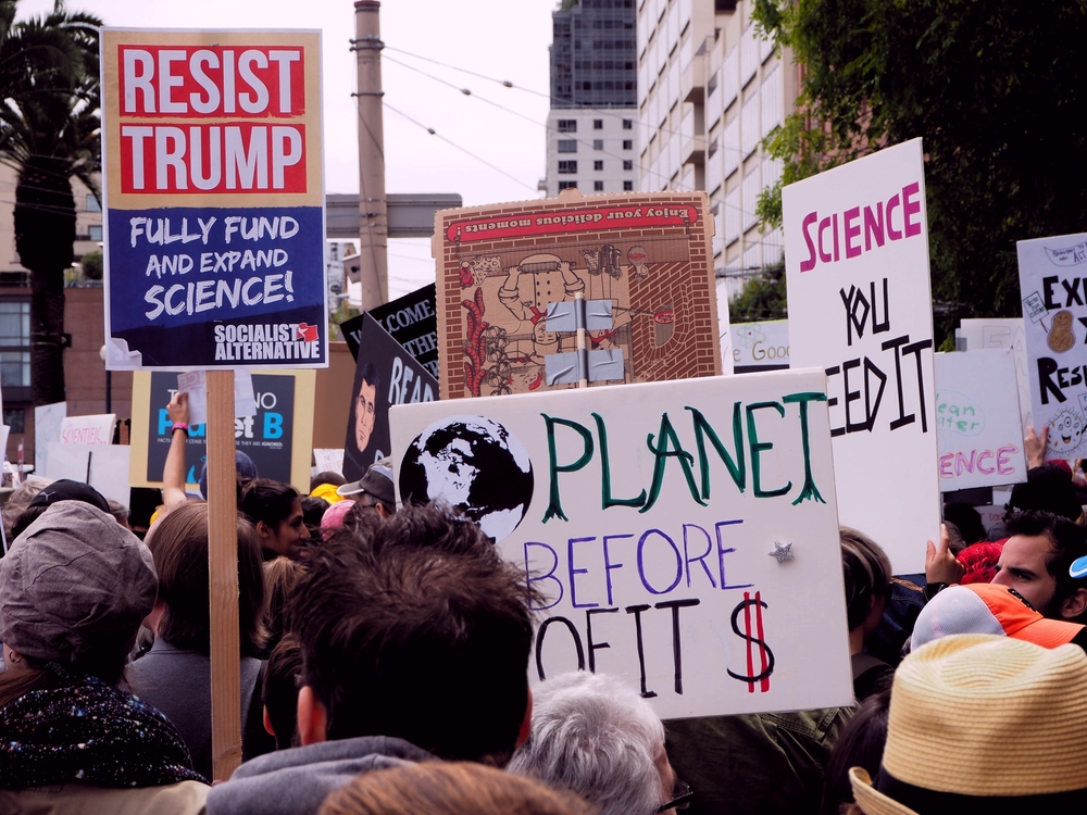 Protest march with signs saying Resist Trump and Planet Before Profits